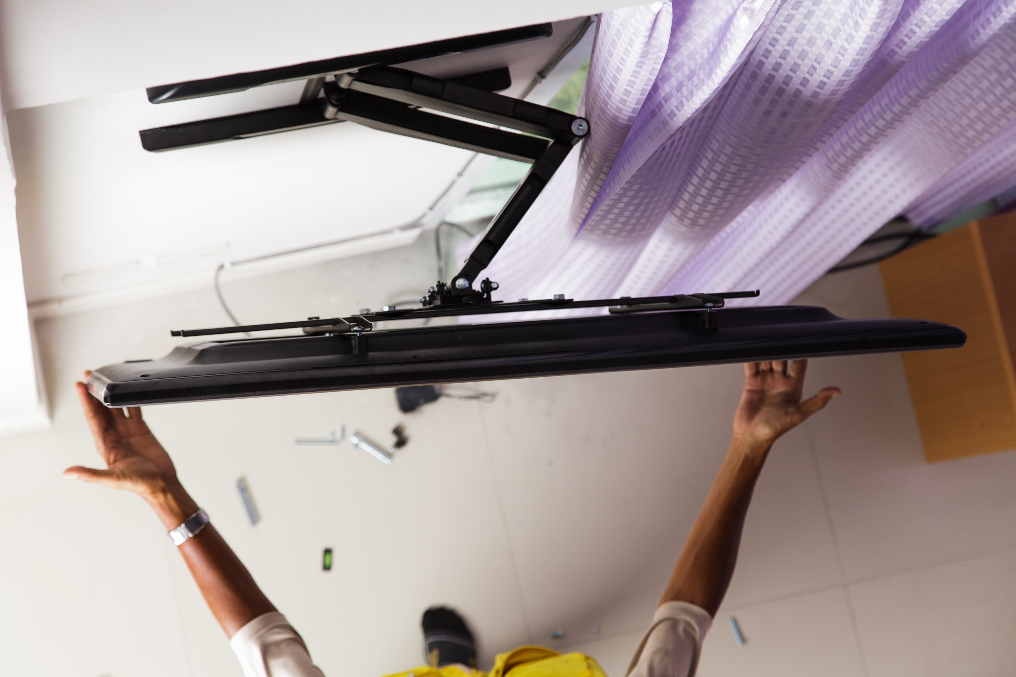 A person mounting an extendable TV bracket to the wall with a TV attached.